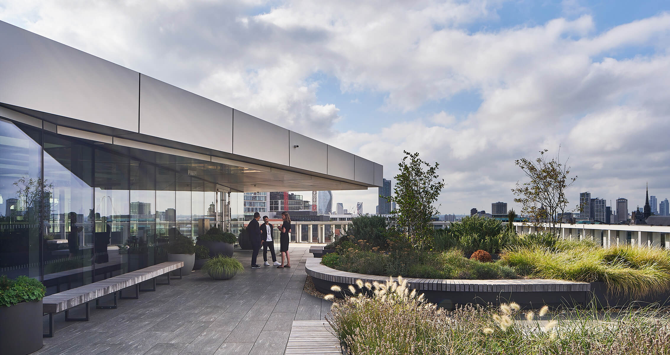 Modern rooftop garden with people and city skyline in the background.