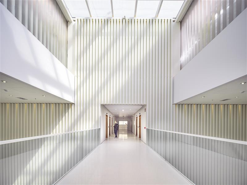 Modern building interior with tall ceilings, natural light, and a person walking down a corridor with doors on both sides.