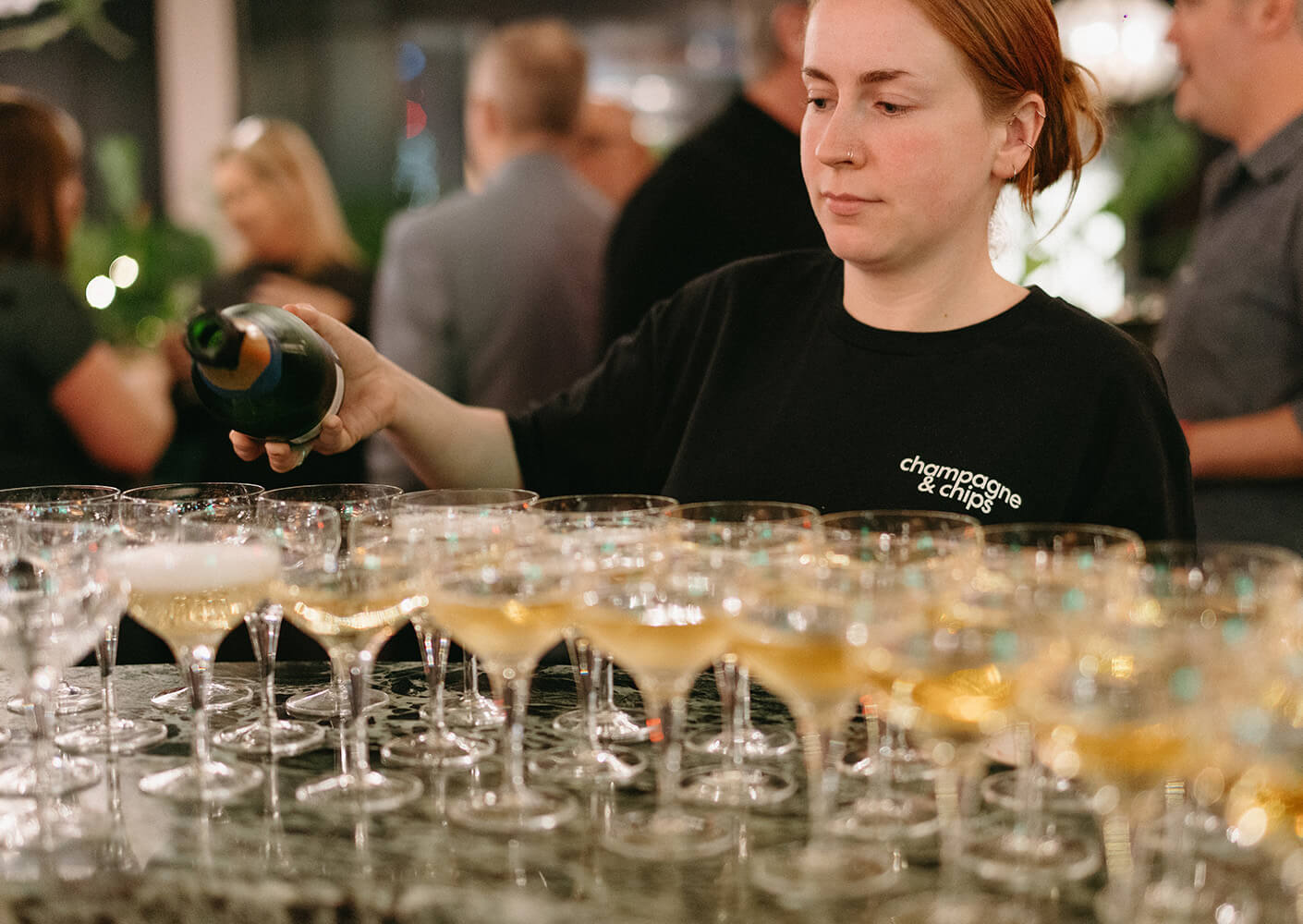 Person pouring champagne into glasses at a lively event.