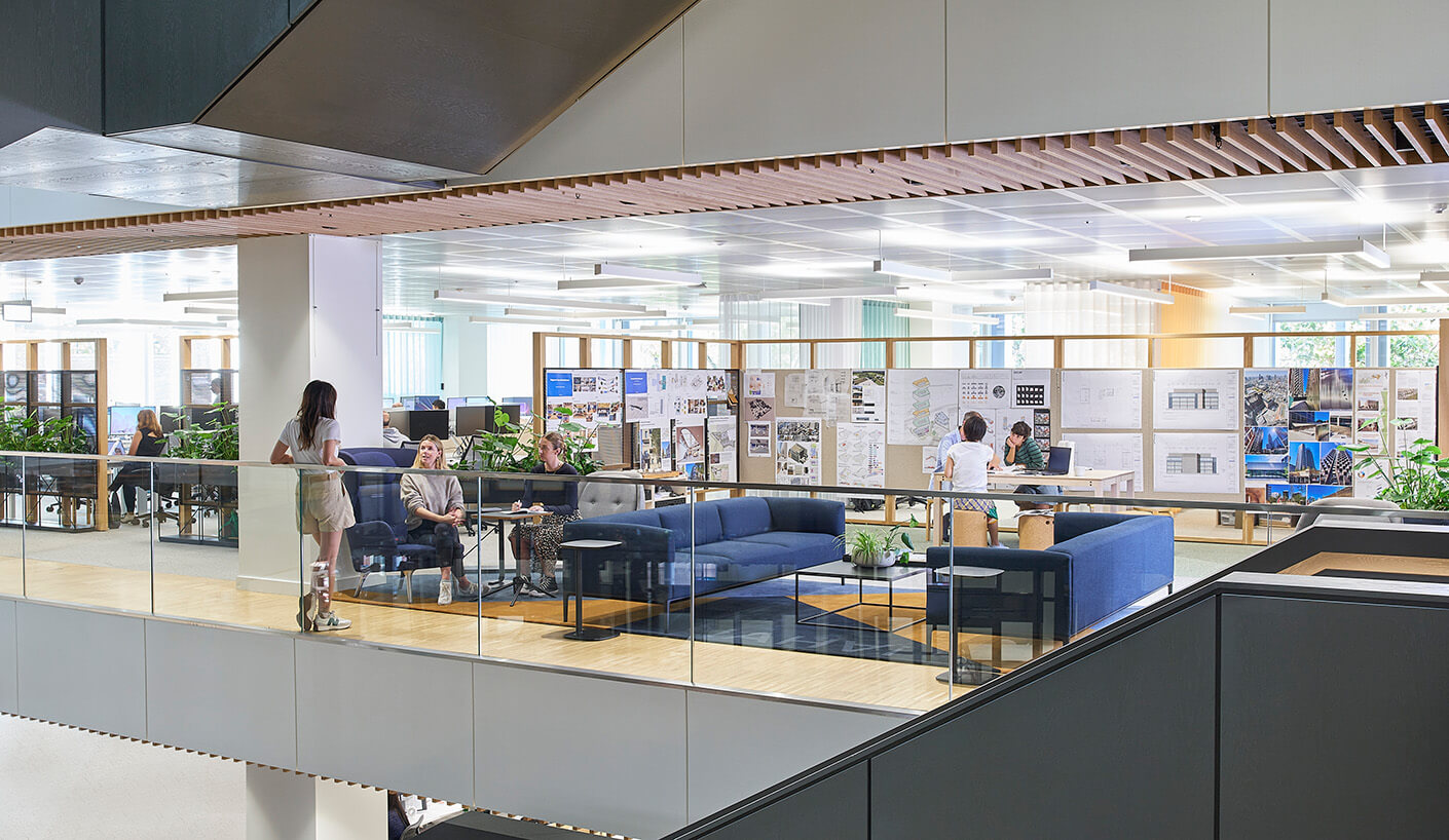 Modern open office with blue sofas, people collaborating near design boards.