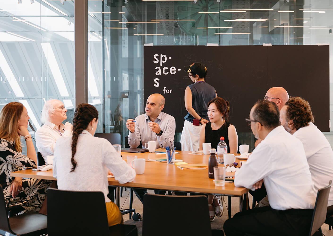 A diverse group of professionals engaged in discussion around a large table in a bright, collaborative workspace.