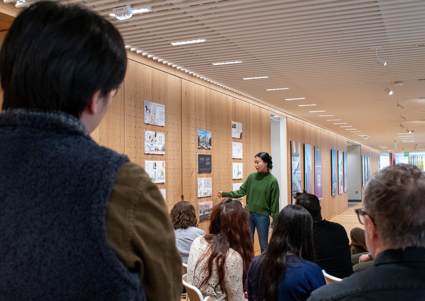Presenter discusses design projects with an engaged audience in a modern exhibition space.