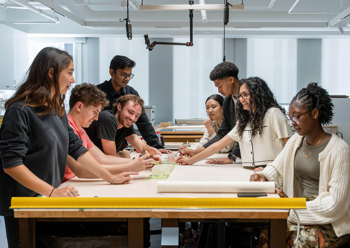 Students collaborate on an architectural project in a well-lit studio, engaging with materials and discussing design concepts.