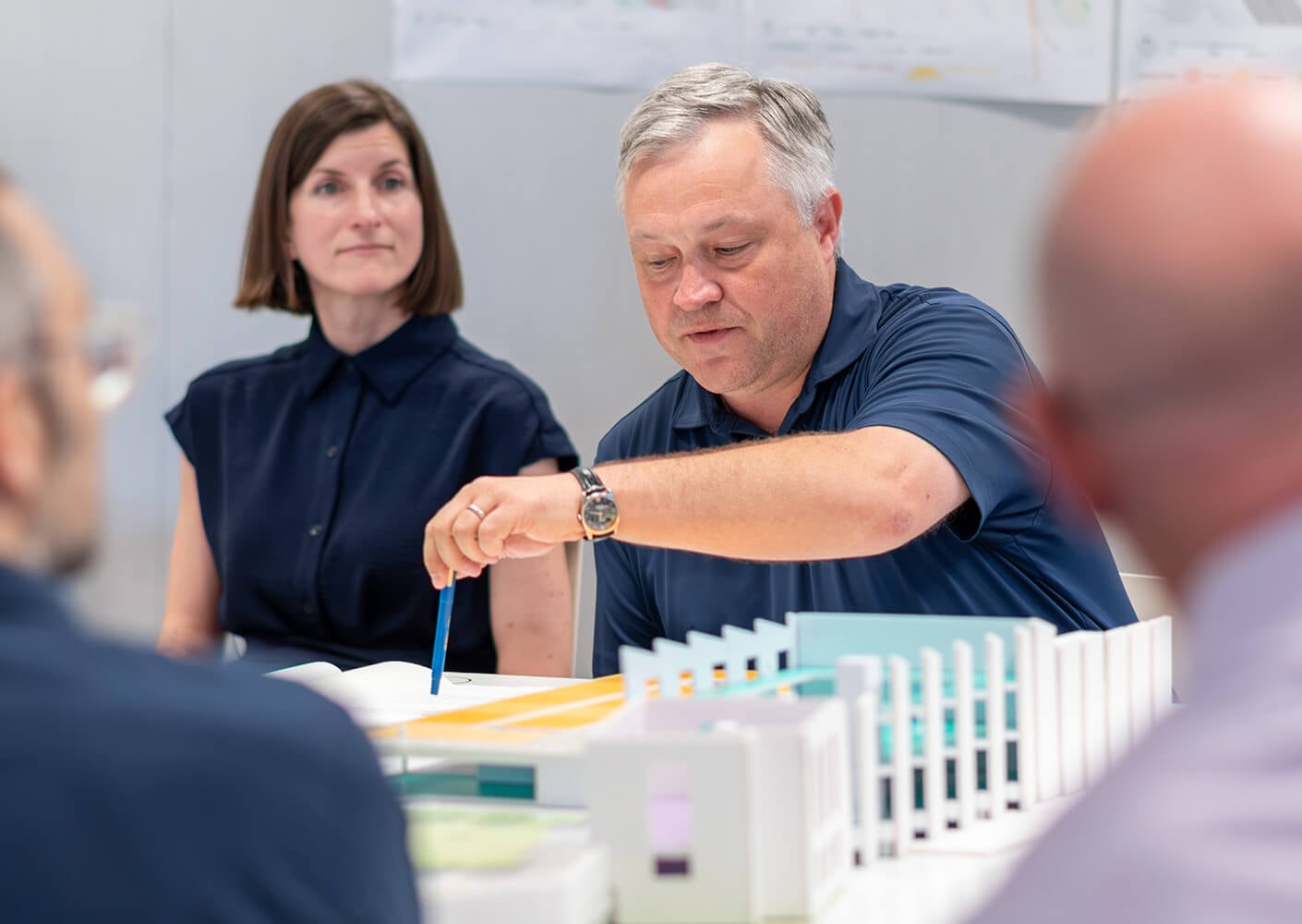 Two professionals discuss a project at a table with architectural models and plans, showing collaboration in design and planning processes.