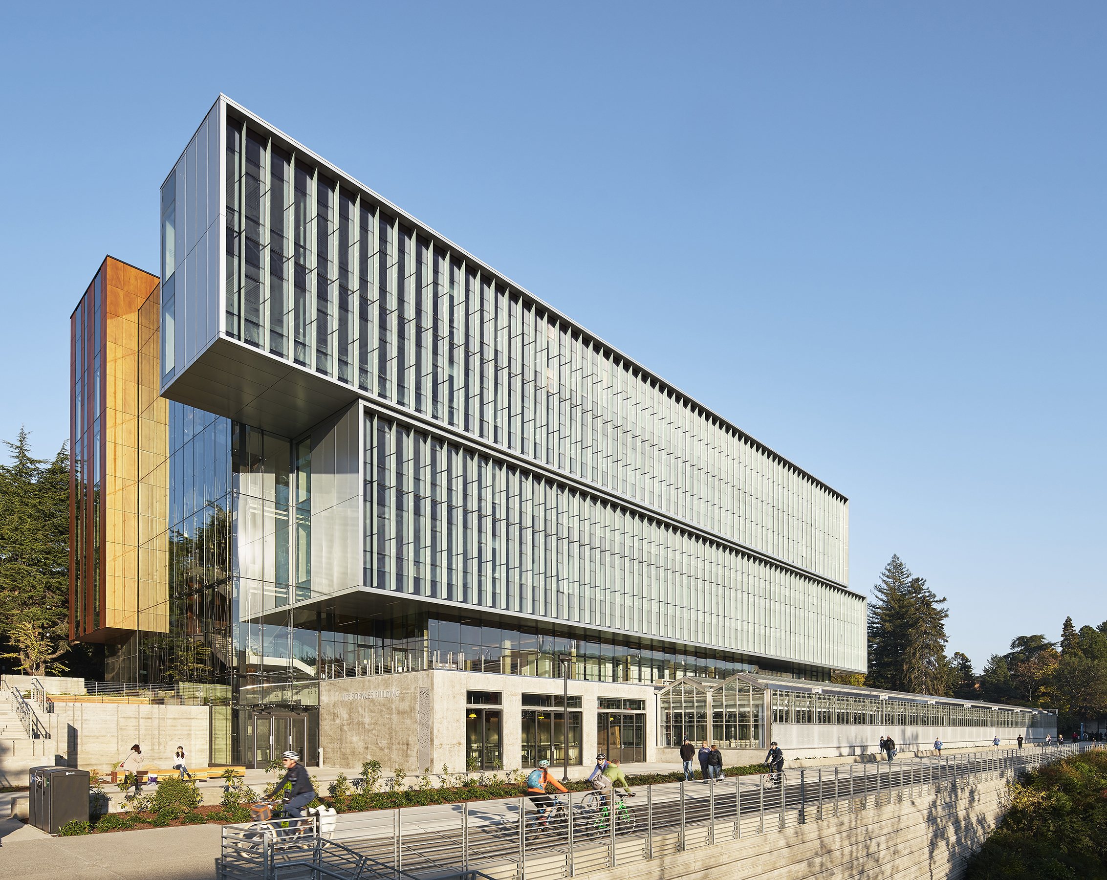 View of the south facade of UW Life Sciences Building with people biking and walking by on the Burke Gilman trail.