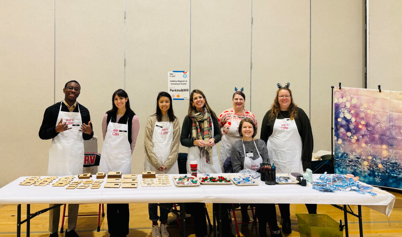 Group of volunteers at holiday craft table with aprons and decorations.
