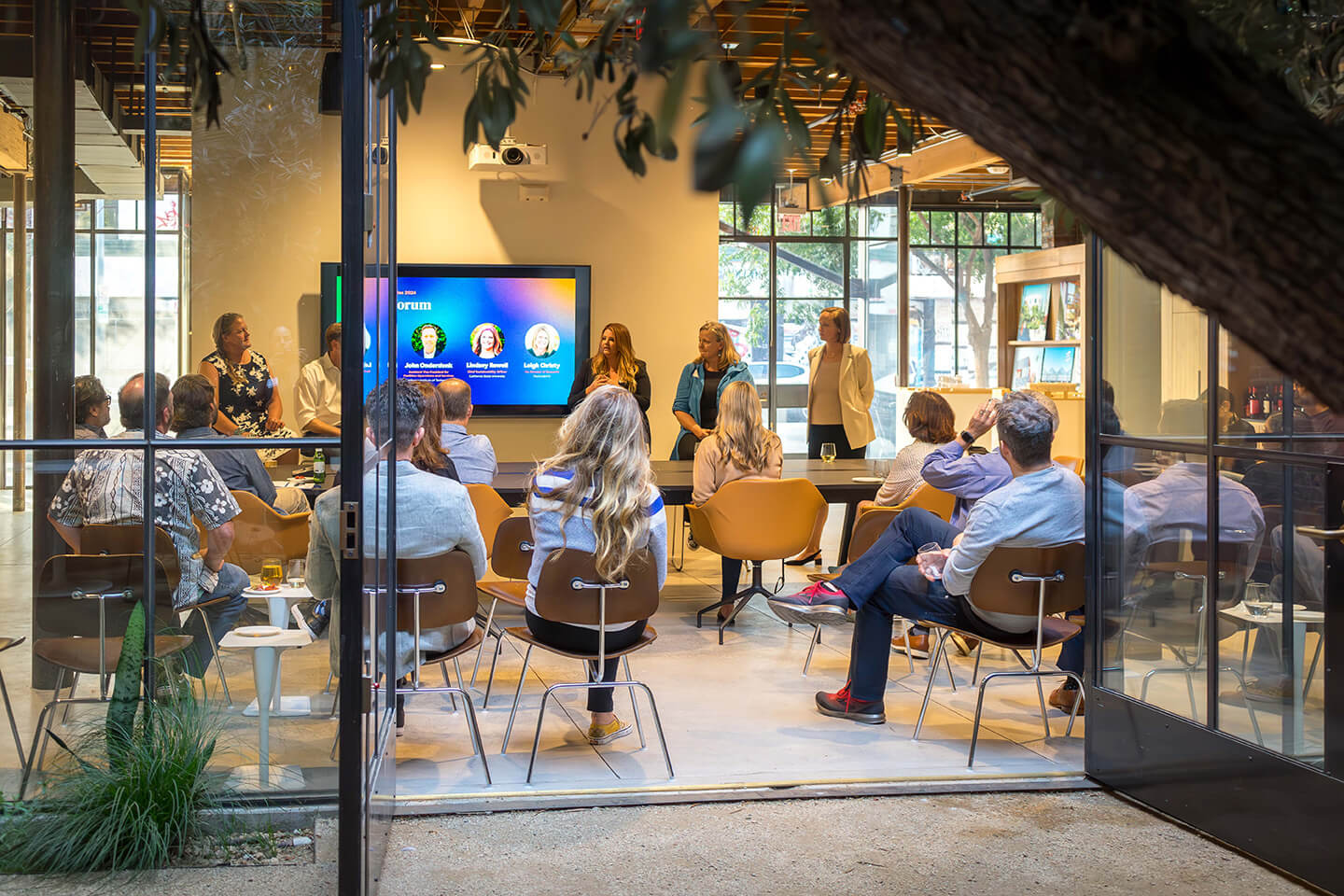 Audience attending a seminar inside a modern glass-walled conference room.