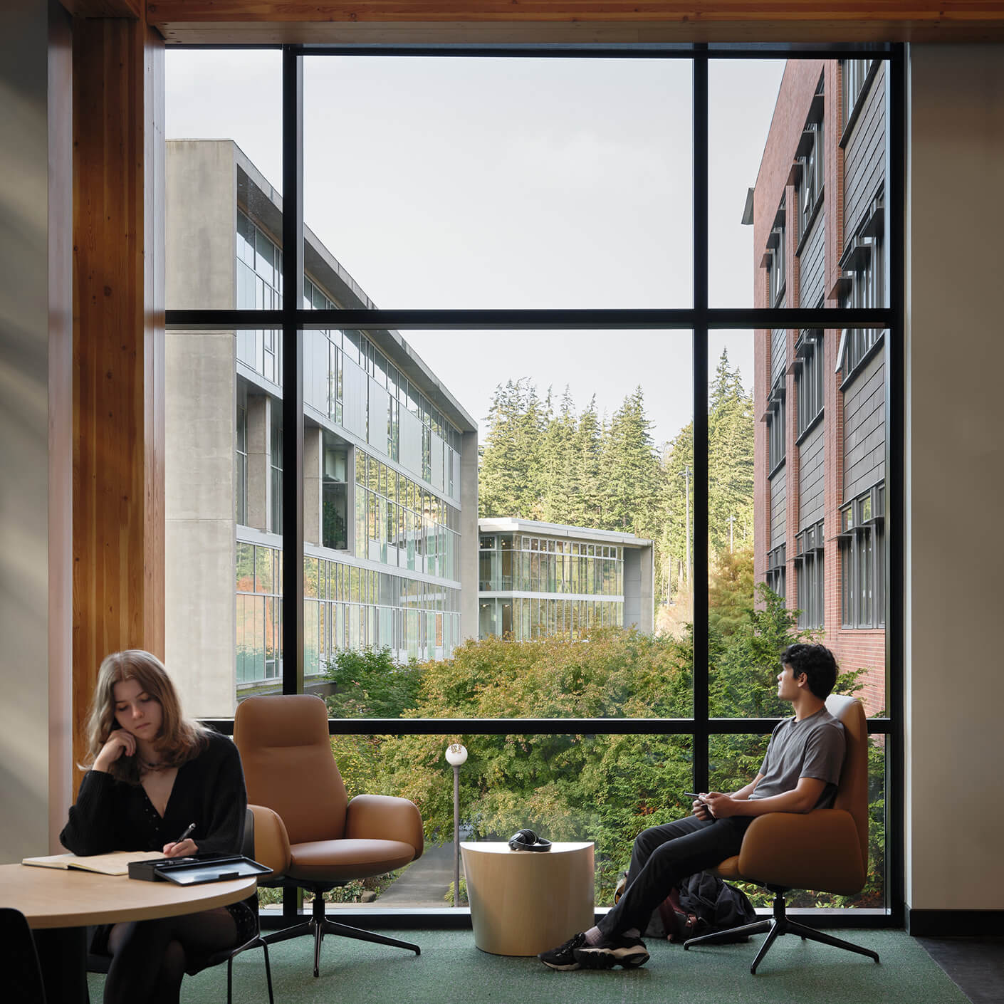 Modern university lounge with large window view of tree-lined campus courtyard.