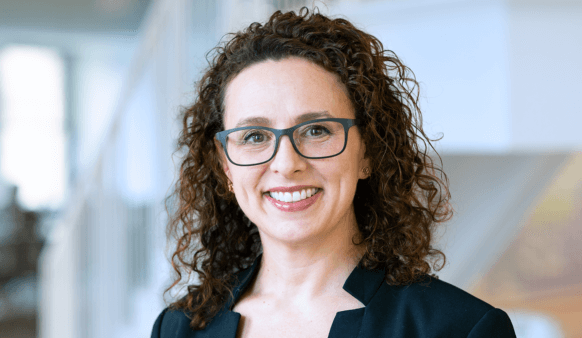 Smiling woman with curly hair and glasses in a professional setting.