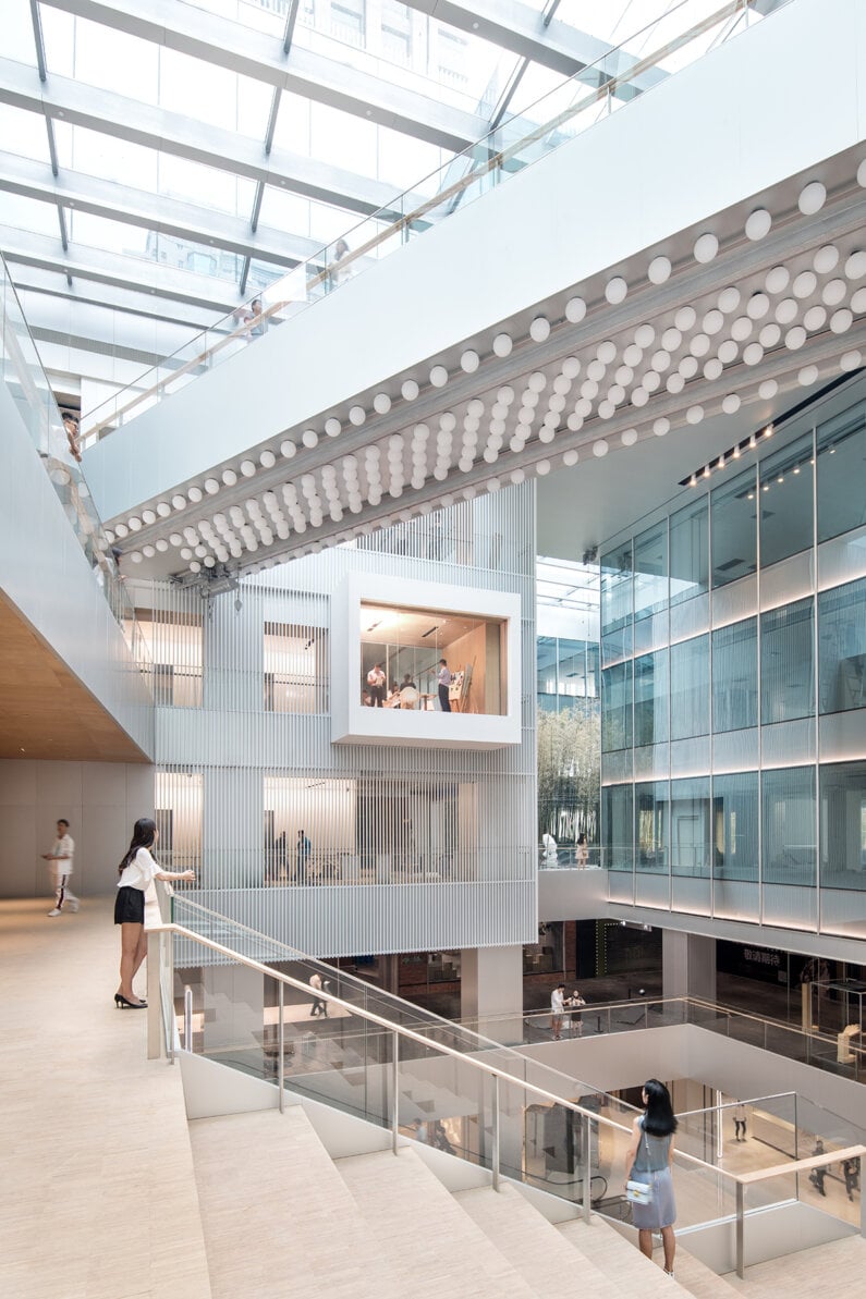 Spacious atrium featuring glass walls, a layered staircase, and unique geometric lighting.