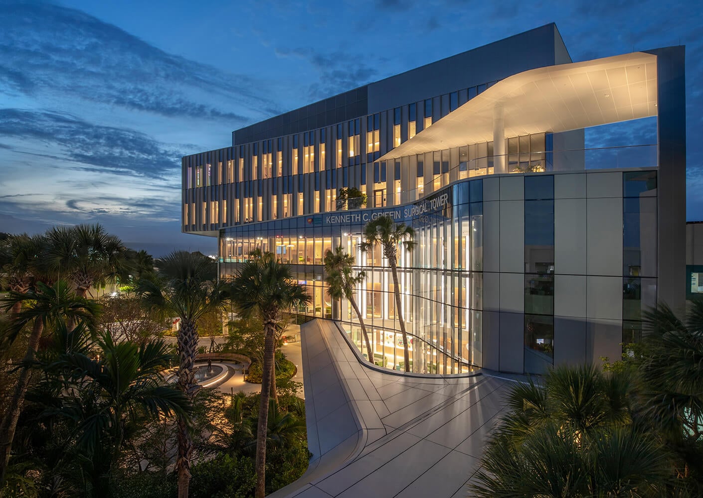 Exterior view of the Kenneth C. Griffin Surgical Tower, featuring sleek design and landscaping with palm trees at dusk.