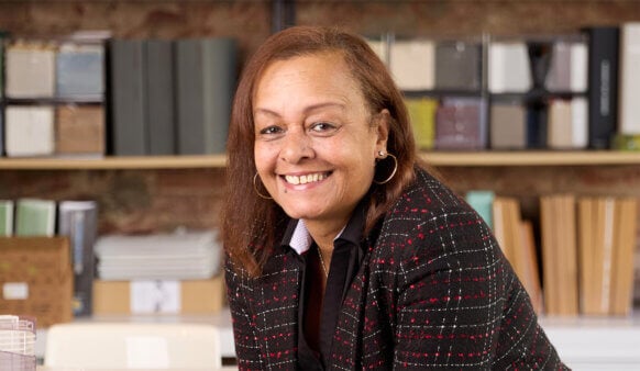 Portrait of a woman smiling in an office setting, with shelves of books and materials in the background.