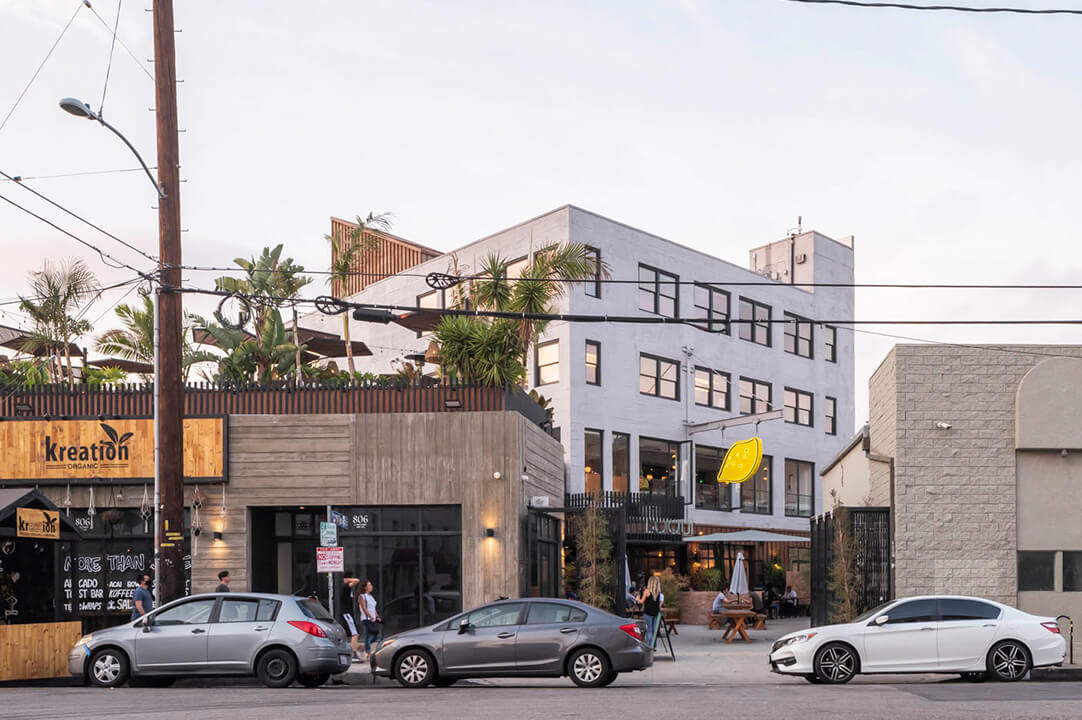 Street view of urban cafe with parked cars and greenery.
