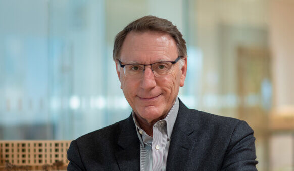 Headshot of Bill Harris, Perkins&Will Northeast Regional Director, smiling in an office setting, wearing glasses and a blazer.