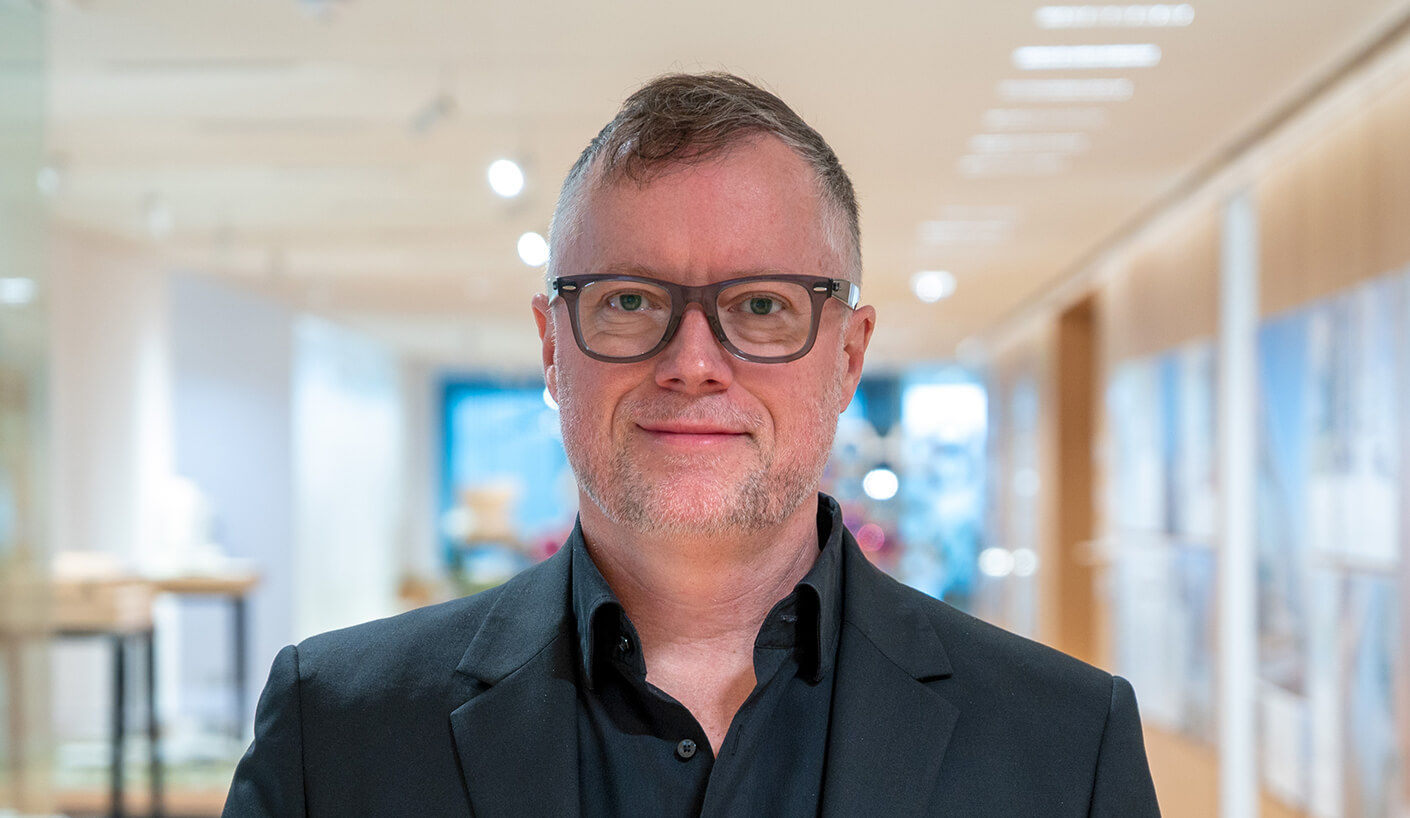 Headshot of Matthew Pierce in a black suit standing in a bright, modern office setting.