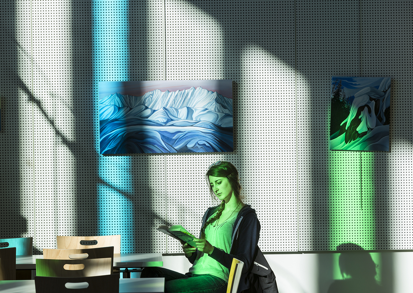 Girl reading at table with bright blue and green shadows casting on her and the wall behind her
