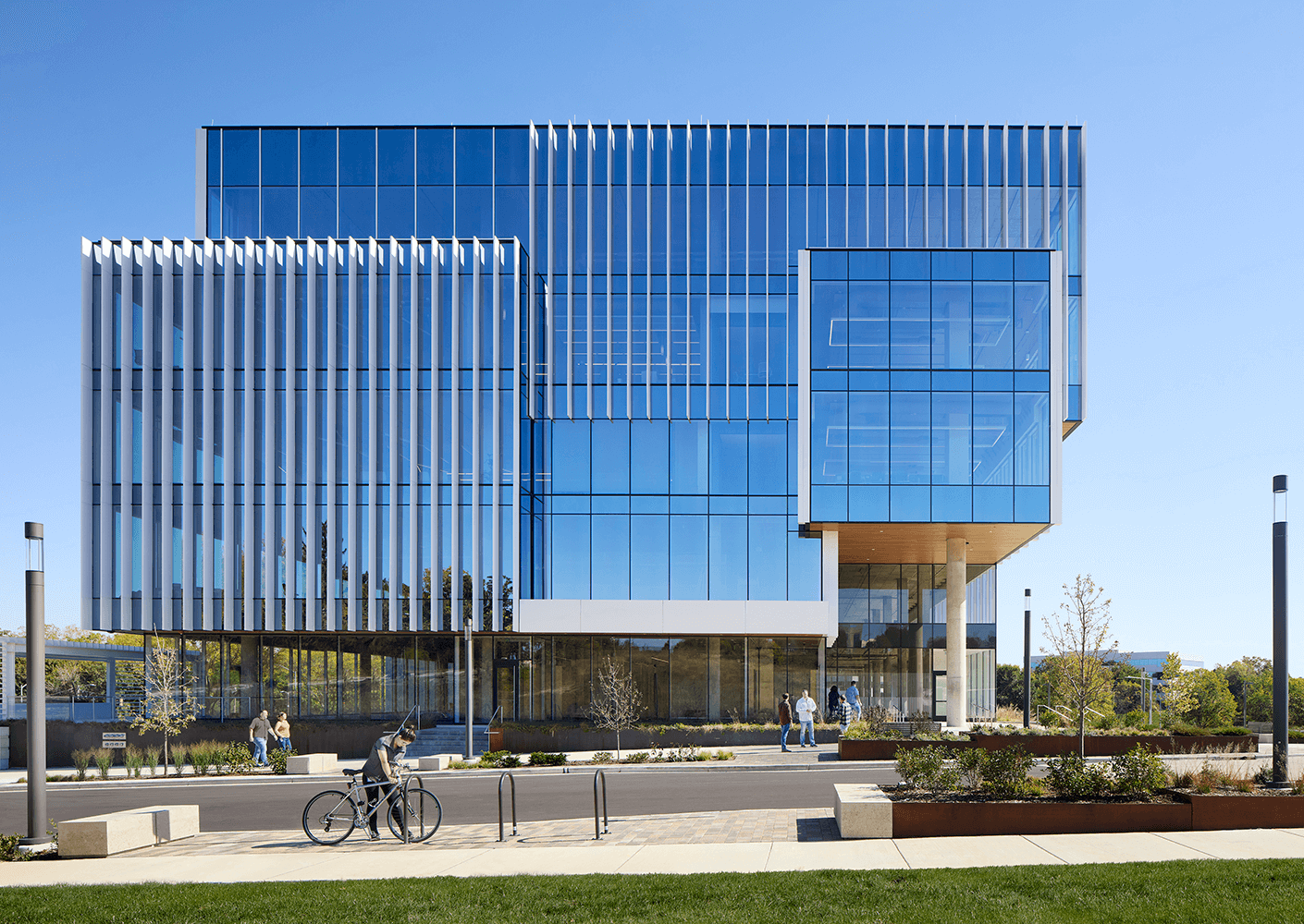 Modern glass building exterior with cyclists and pedestrians nearby.