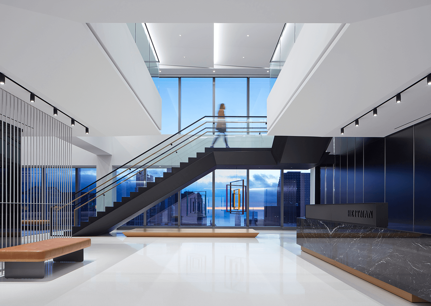 Modern office lobby with staircase and city view through large windows.