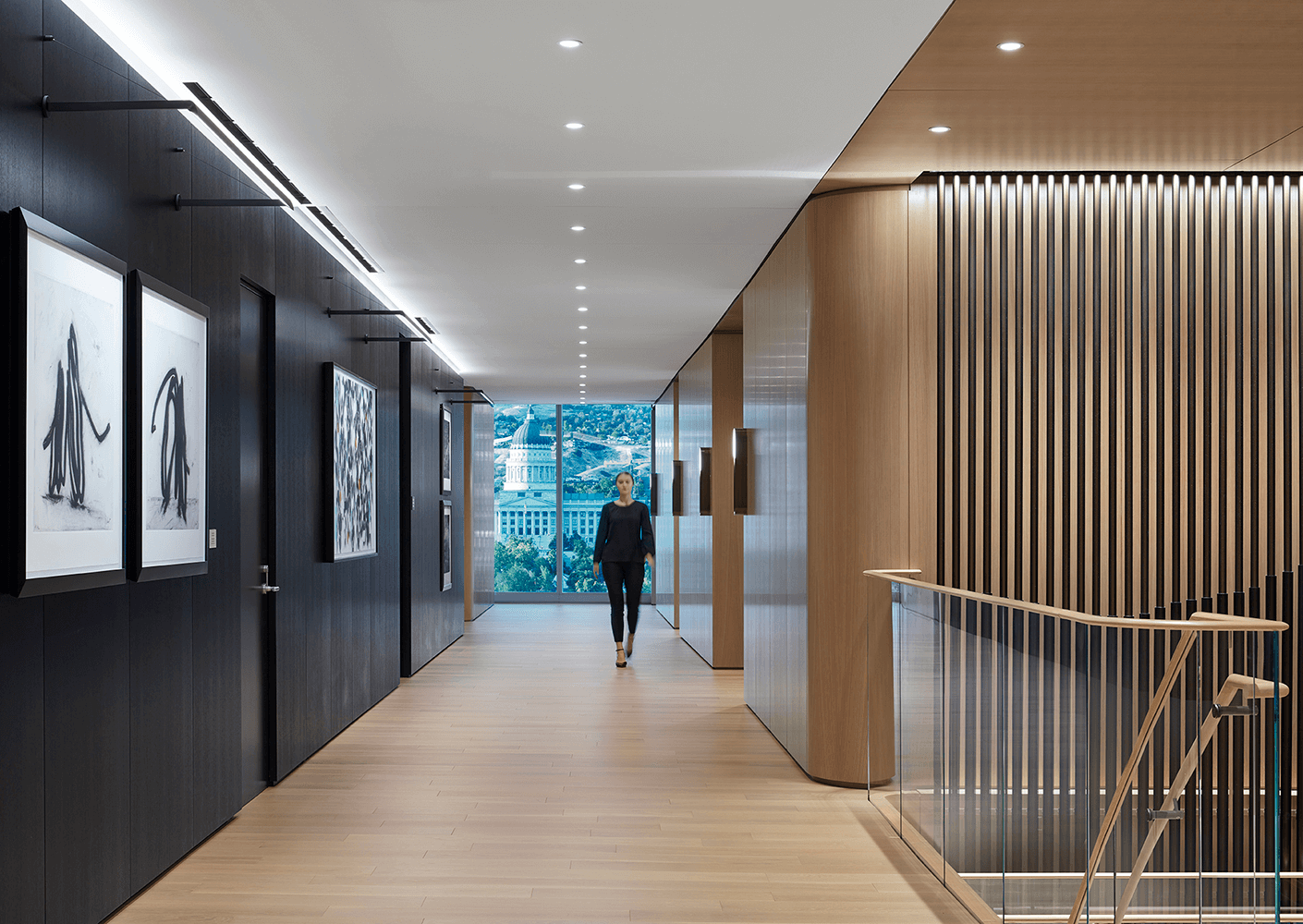 Modern office hallway with art, person walking, and city view.