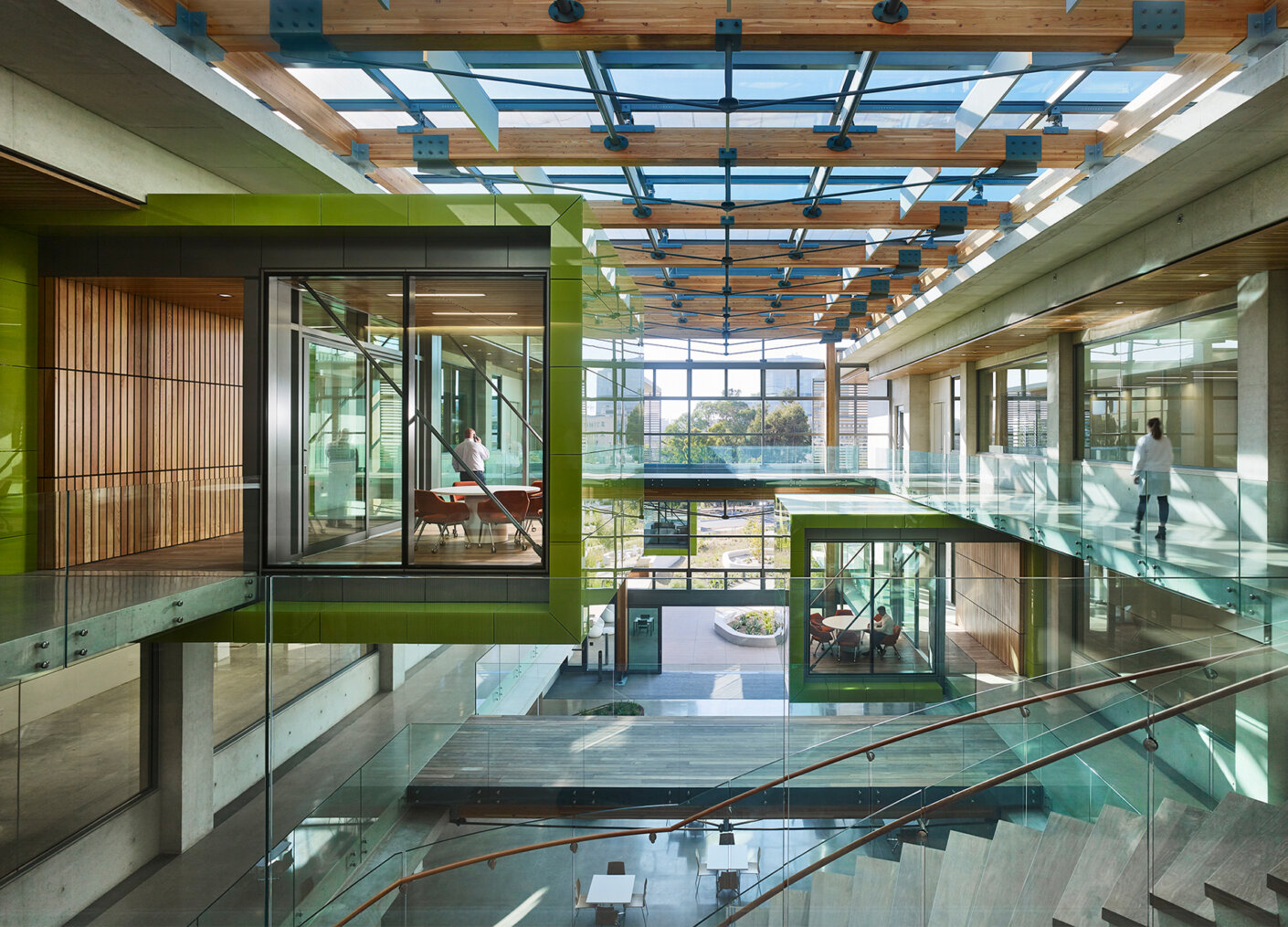 Two green meeting pods hang into atrium with large glass ceiling above.