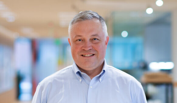 Headshot of Derek Johnson, Perkins&Will Boston Corporate and Commercial leader, smiling in an office setting, wearing glasses and a blazer.