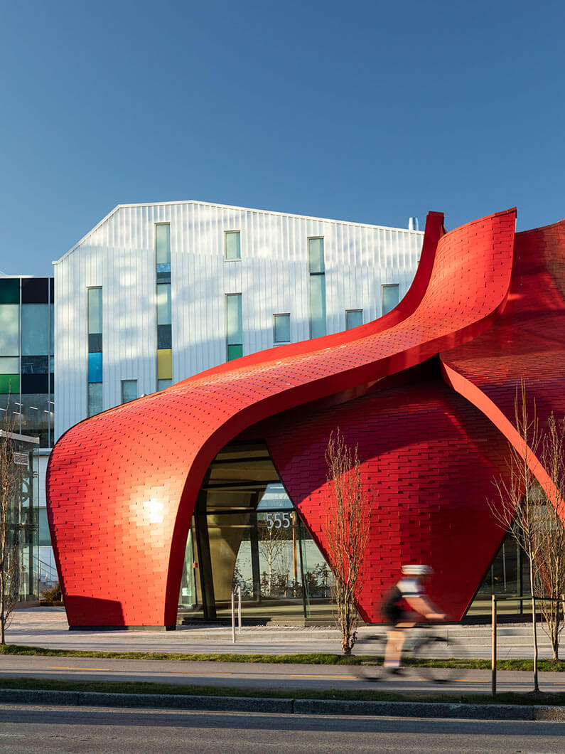 Photo showing the red curved petals of the pavilion with Emily Carr University in the background.