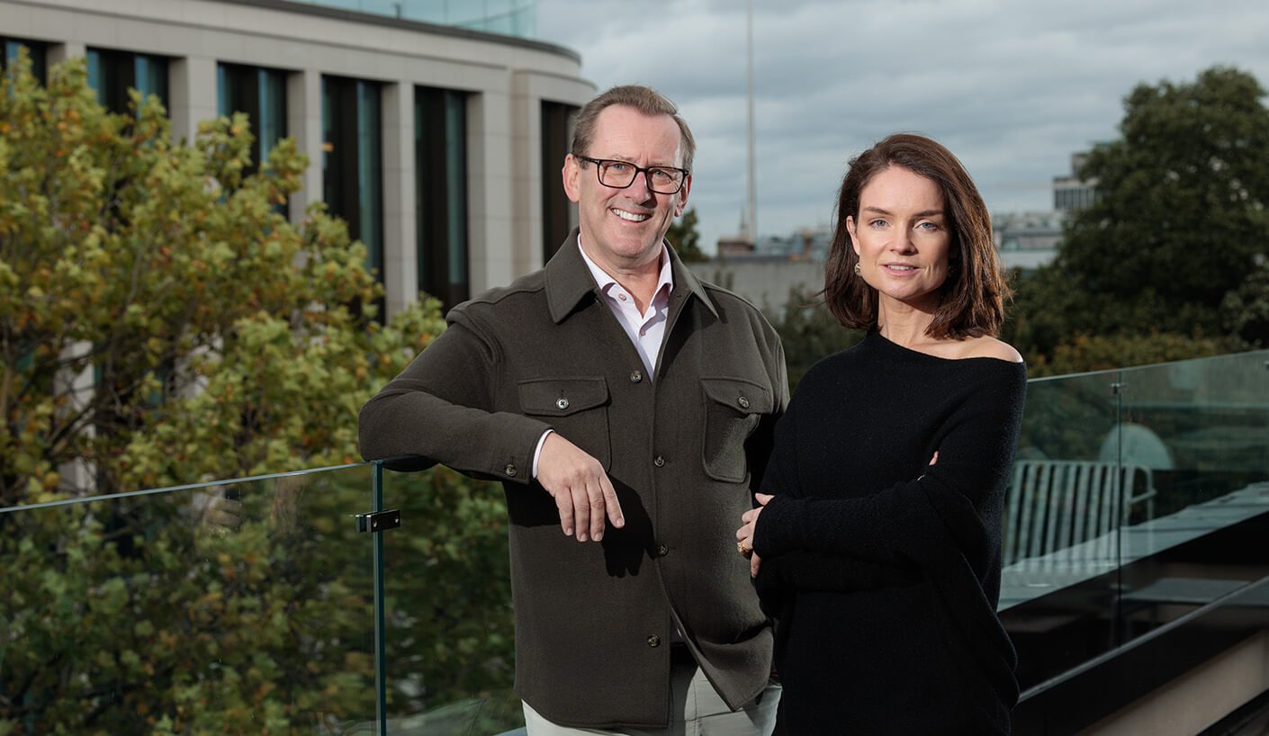 Two people posing on a rooftop with trees and buildings in the background.
