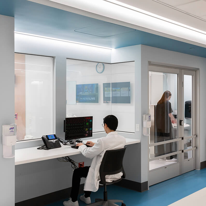 Medical professional monitoring patient vitals on computer screen in modern hospital room.