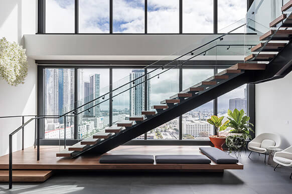 Modern loft interior with glass staircase and city skyline view.