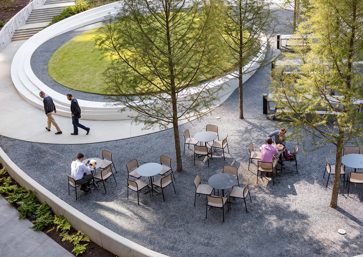 People gather and work at the outdoor seating arrangements by the courtyard's elliptical lawn