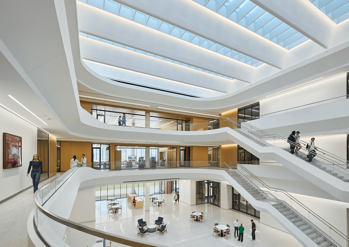 Interior view of a multi-level building featuring open spaces, staircases, and people interacting in a bright, well-lit environment.