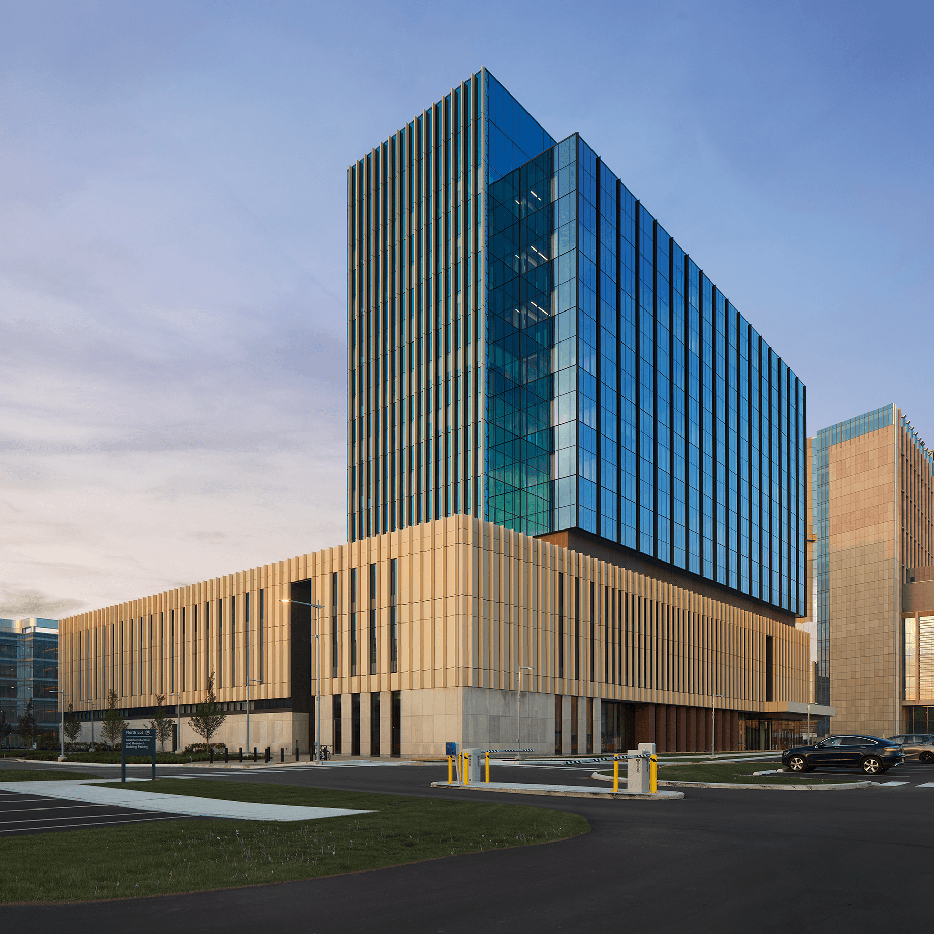 Exterior view of a multi-story office building featuring glass and stone facades, with landscaped surroundings and parking area.