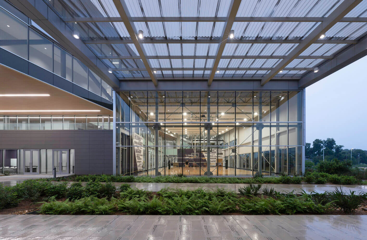 Modern glass building exterior with greenery and view inside to a basketball court.