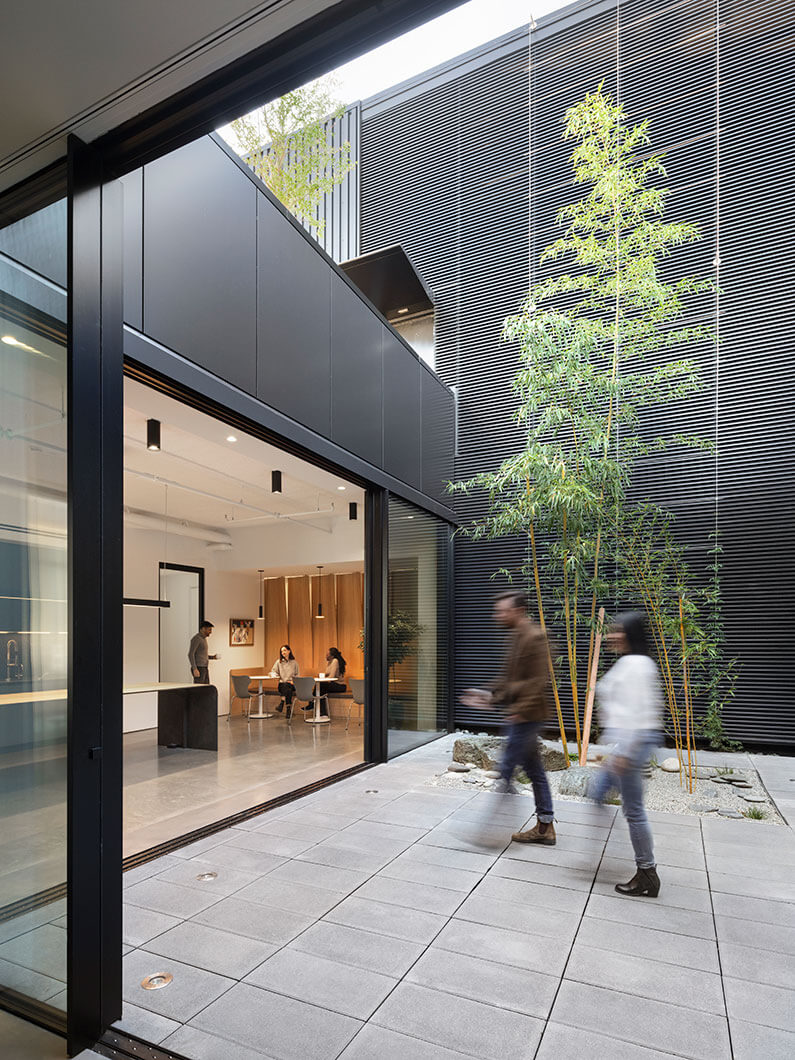 Photo of people walking in an outdoor courtyard that opens to an interior office space with moveable glass walls.
