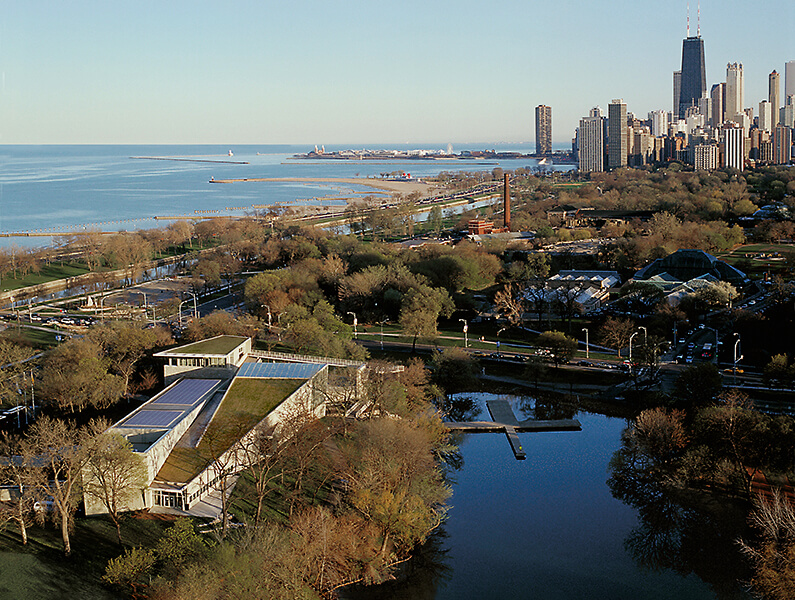 An aerial view of the Chicago Academy of Sciences Peggy Notebaert Nature Museum between the river and the lake with the skyline in the distance