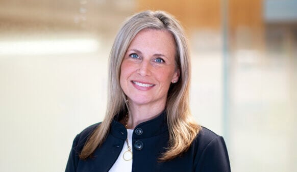 Headshot of Abby Gillespie smiling, wearing a black jacket, in a bright office setting.