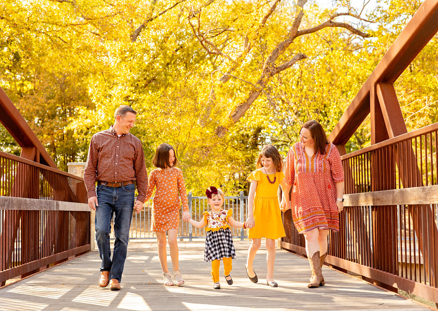In this family portrait, Brad and wife and daughters smile at one another in front of a vibrant autumn scene