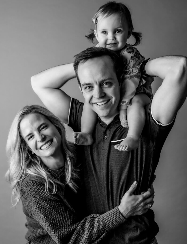 Sarah smiles with her husband and daughter in a family photoshoot