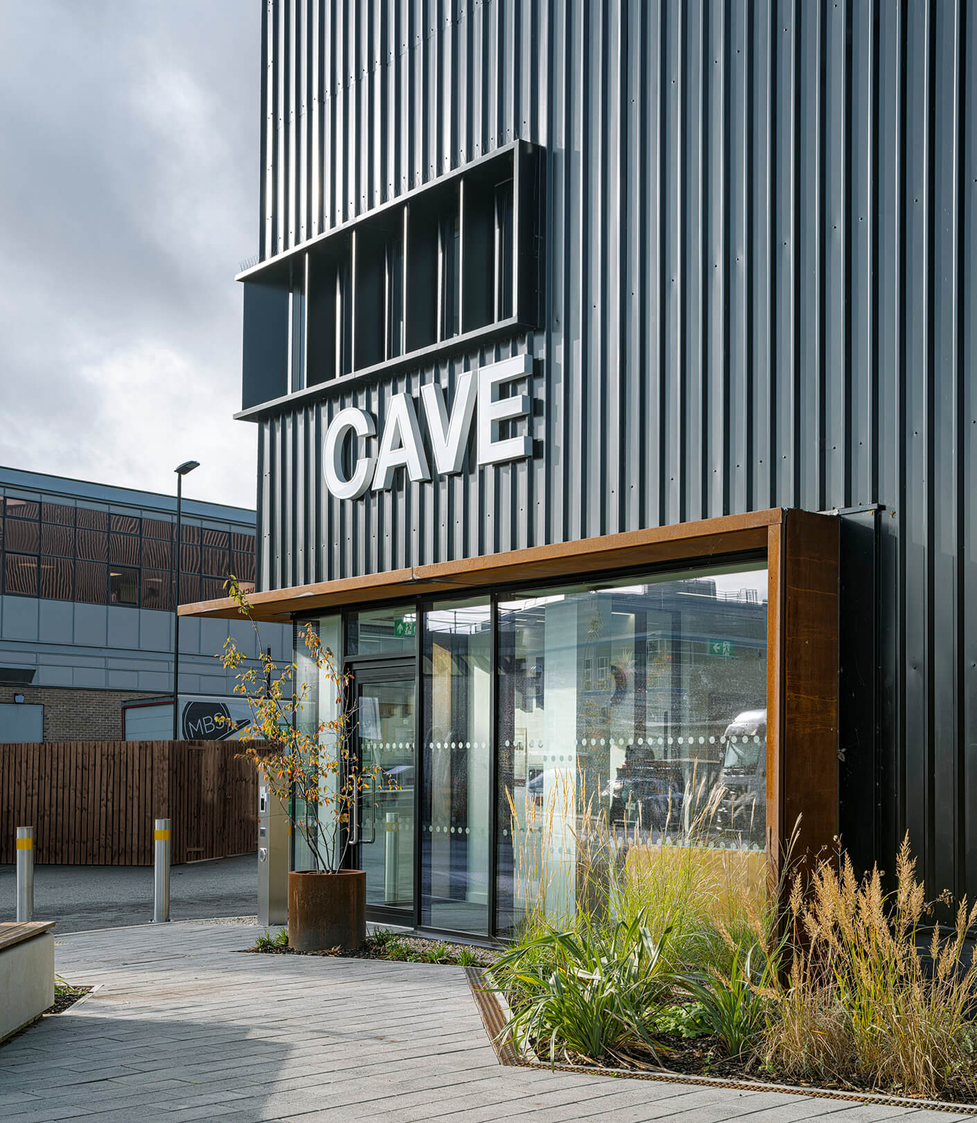 Black exterior with the main entrance door to the CAVE building. The word CAVE is above the doorway and there is exterior plants.