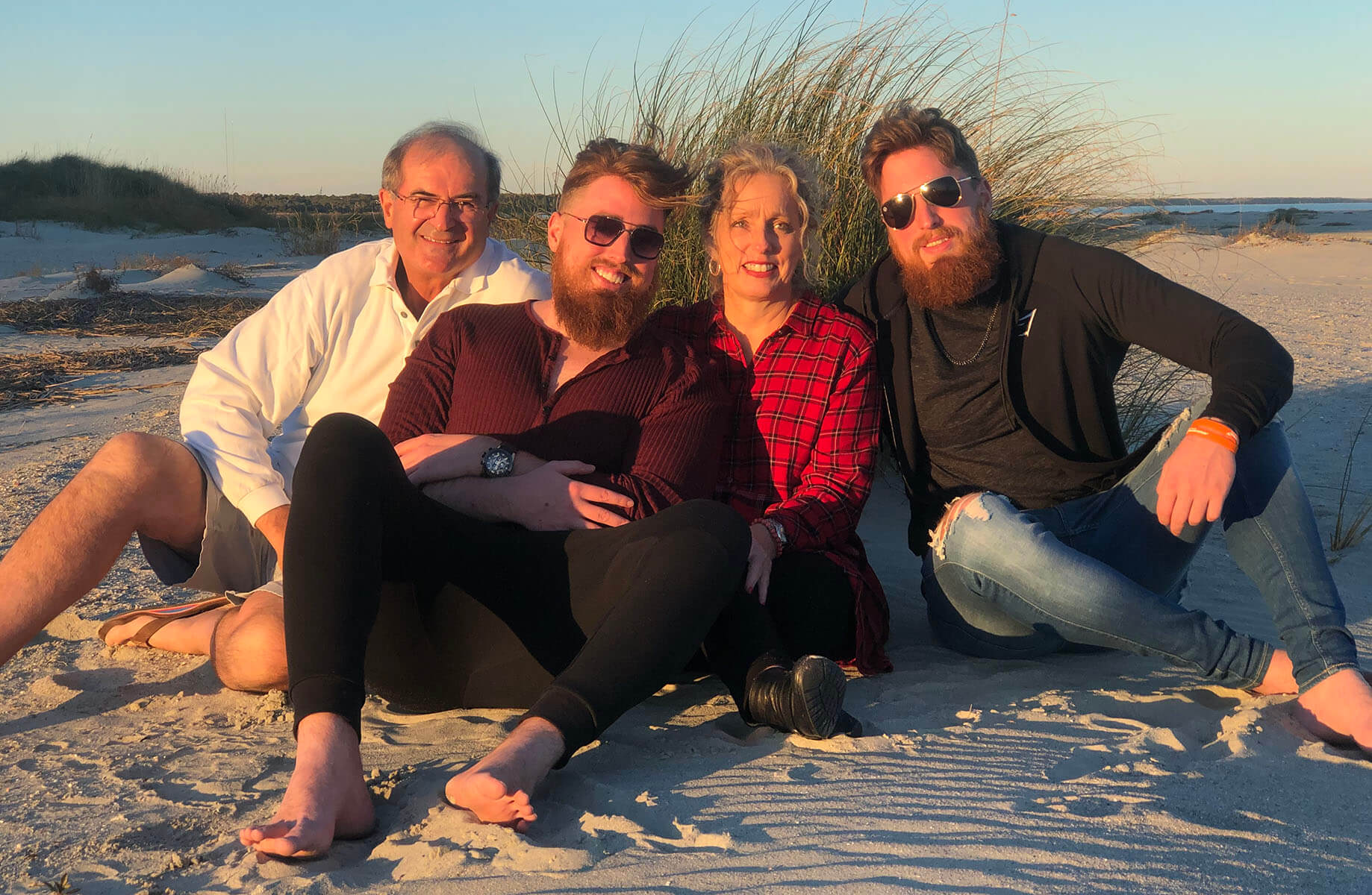 Debbie with her husband and two adult sons smiling at the beach.