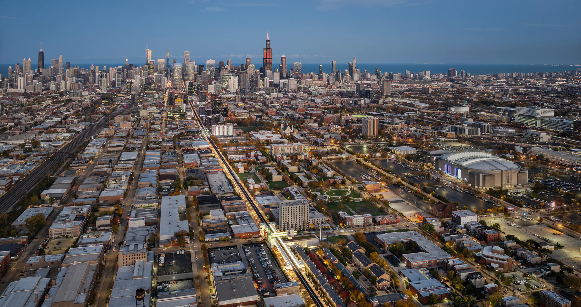 Aerial view of Chicago skyline at dusk with illuminated streets and Lake Michigan in the background.