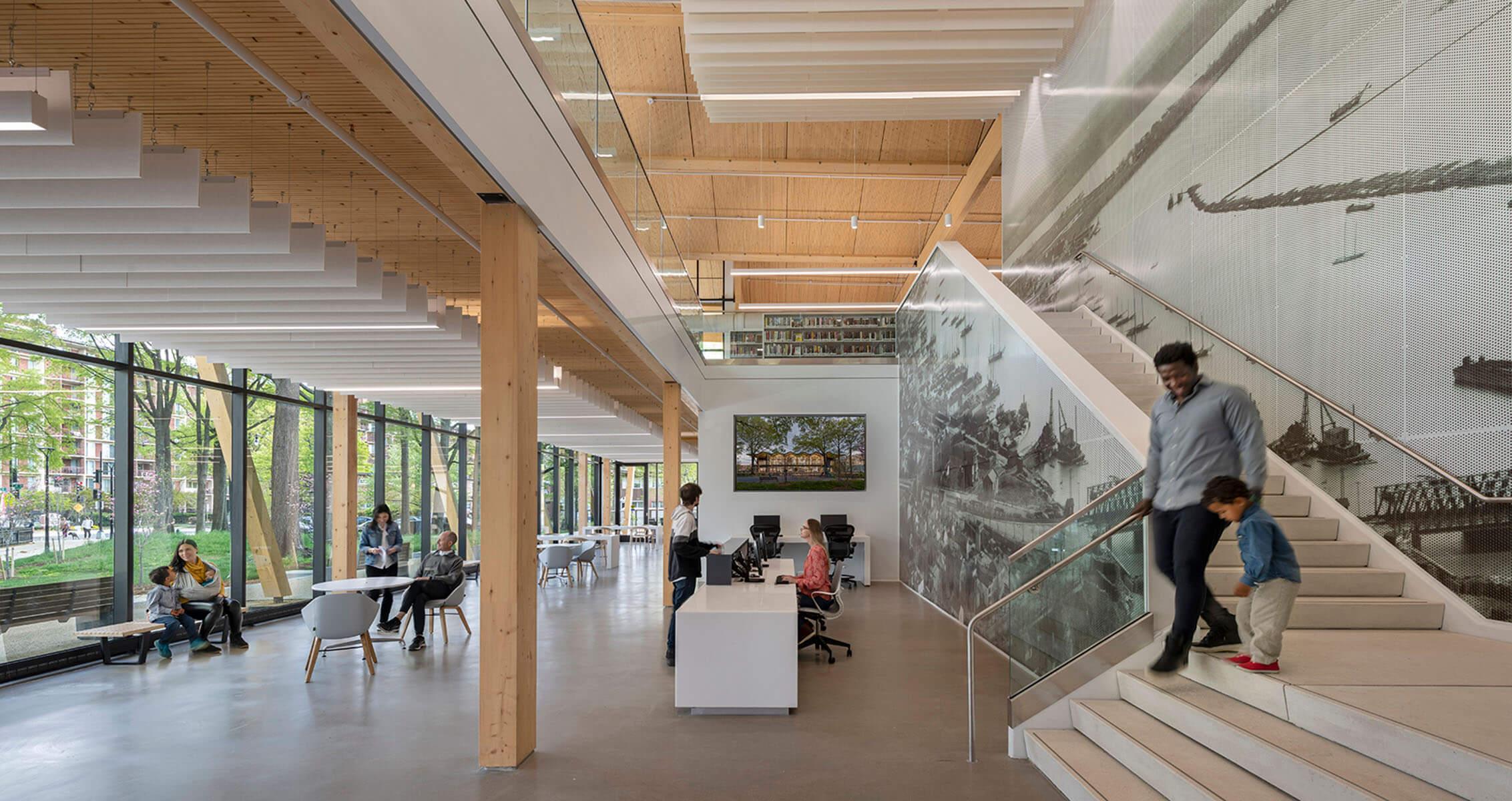 A person and child walk down stairs in a bright atrium with wood accents