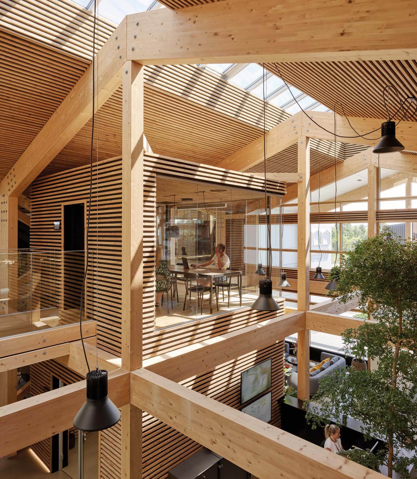 A two-story atrium clad entirely in wood, with an elevated glass walkway and workspace