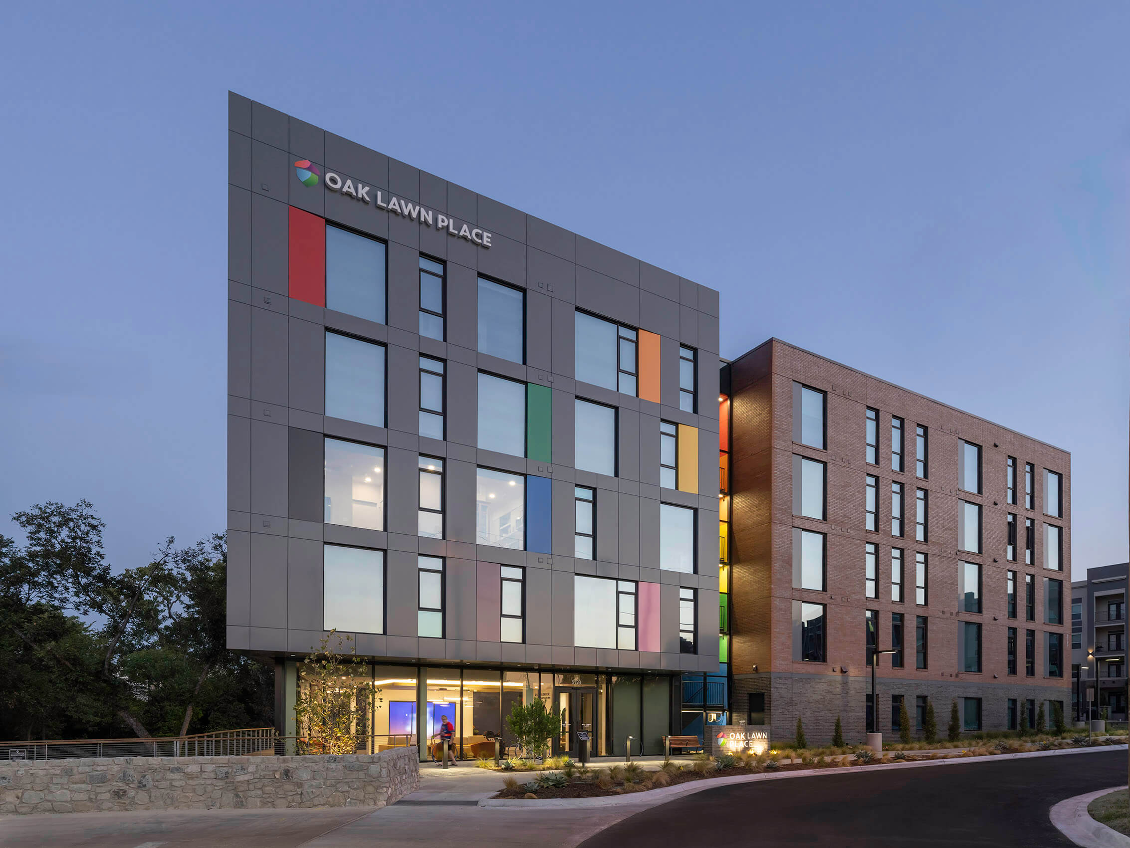 the colorful corner facade of Oak Lawn Place at dusk with a rainbow staircase illuminated