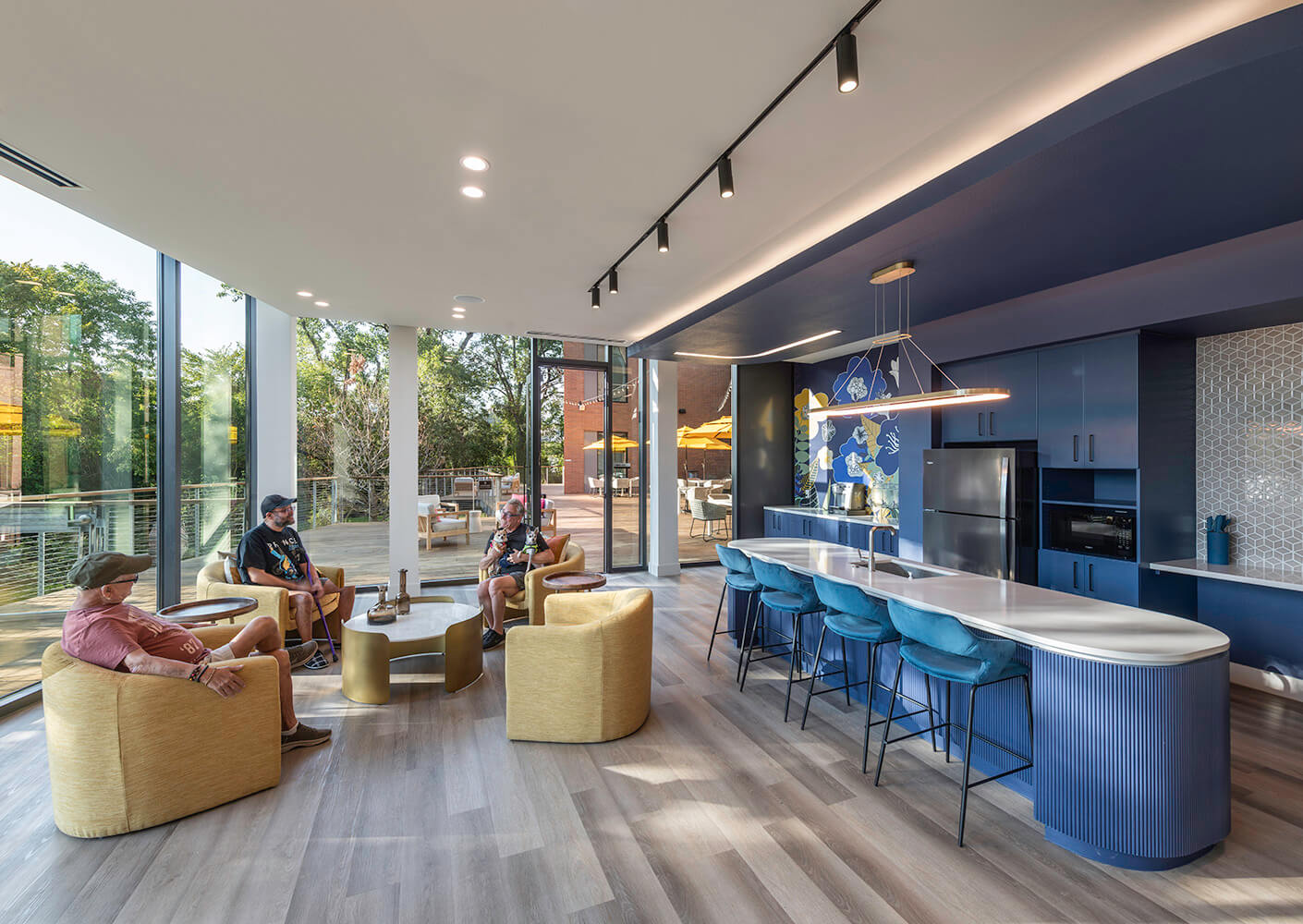 Three residents socialize in the community lounge, featuring a mural and floor-to-ceiling windows.