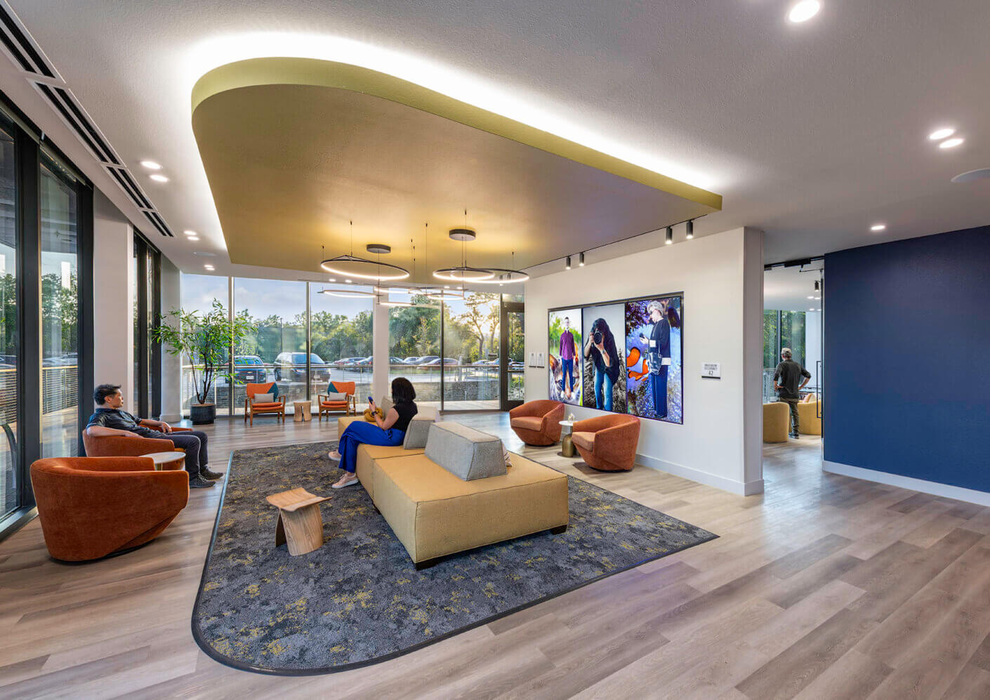 People chatting in a brightly lit community room with floor to ceiling windows and digital art displays