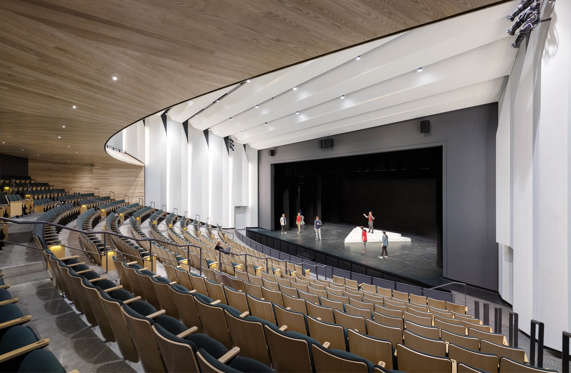 a high school auditorium with undulating white paneling and a mezzanine