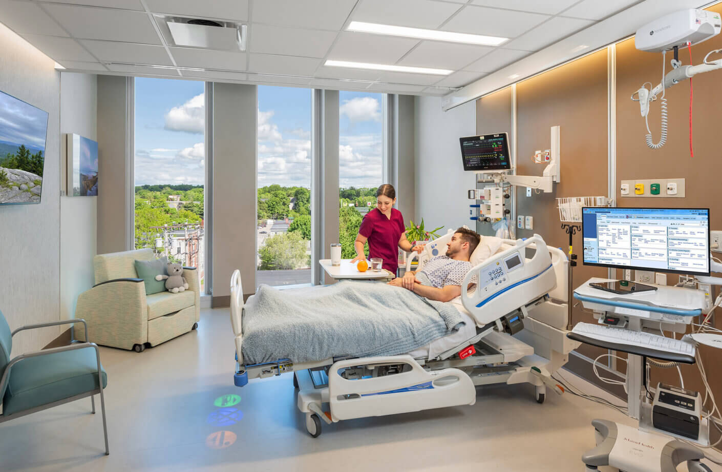 patient room in hospital with patient in bed and nurse helping