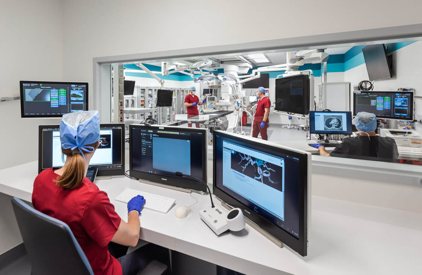 nurse at computer station, looking through window to operating room