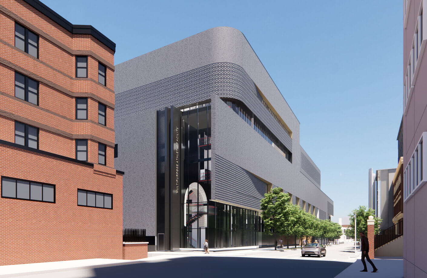 exterior of gray brick sports building with trees and brown brick buildings adjacent